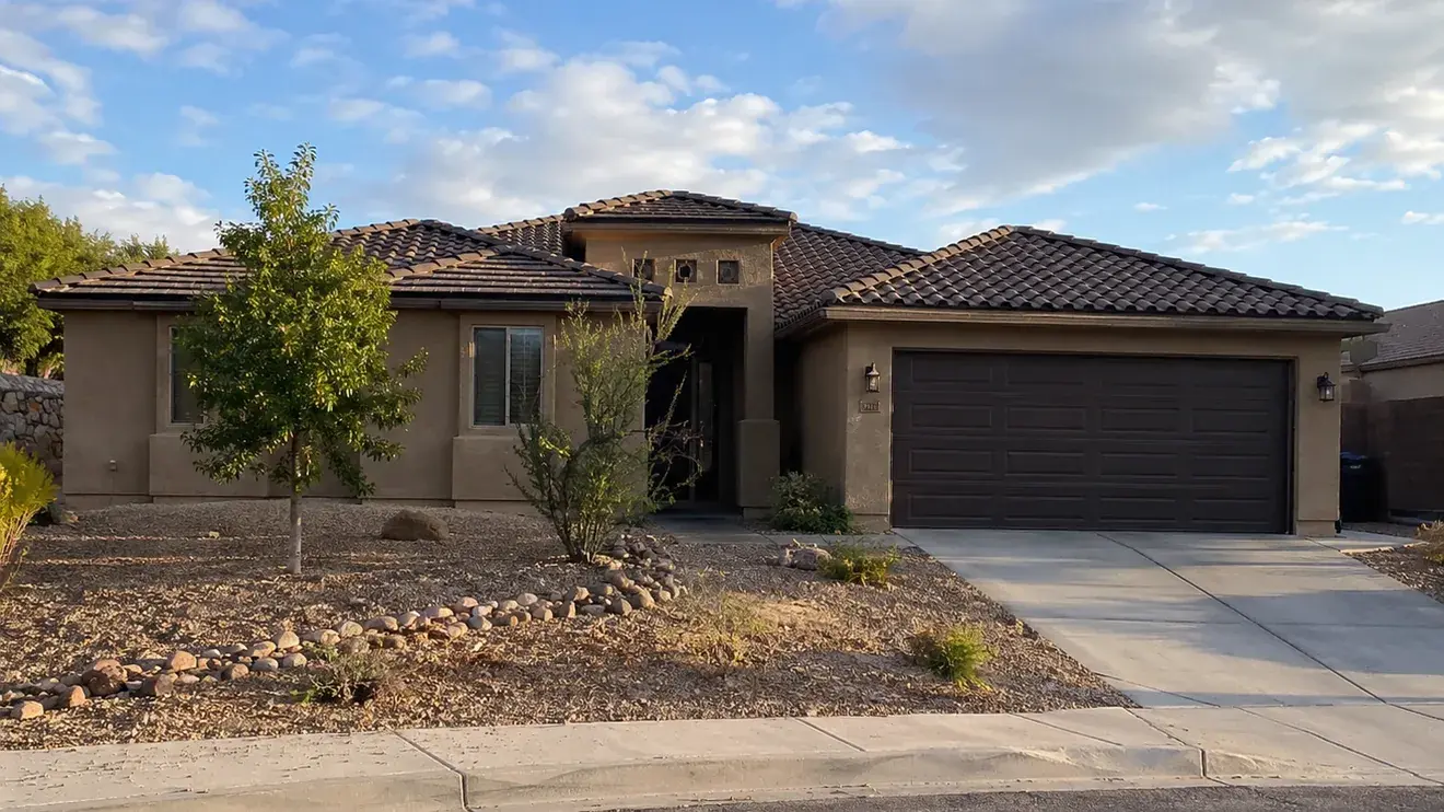 Single-storey stucco home with a brown concrete tile roof and desert landscaping, photographed in late afternoon light