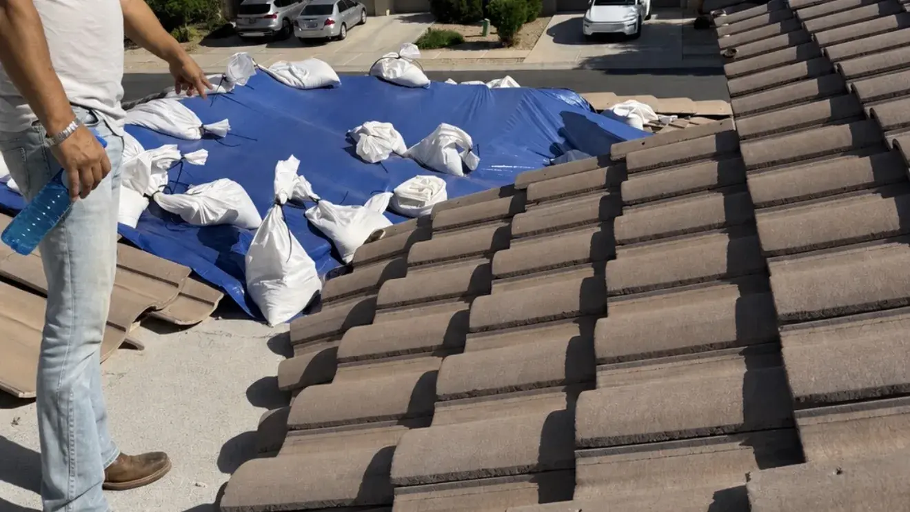 Concrete tile roof with a section of tiles lifted and stacked aside and a sandbagged tarp covering the exposed deck area