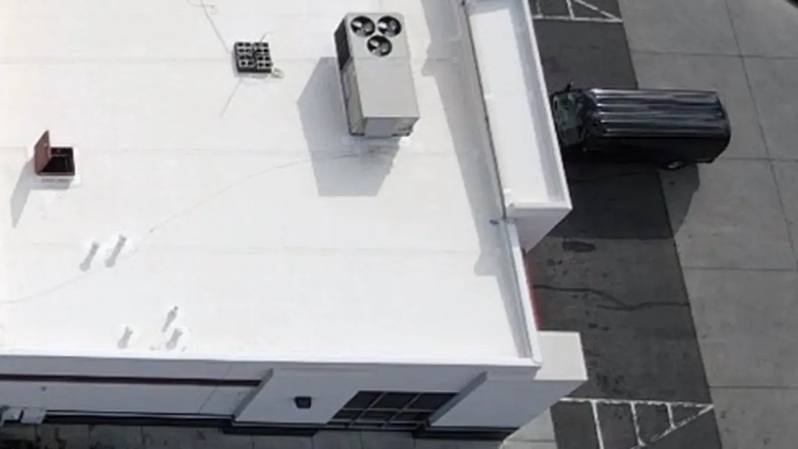 Overhead view of a white flat membrane roof on a commercial building with rooftop units, drains and a parapet edge