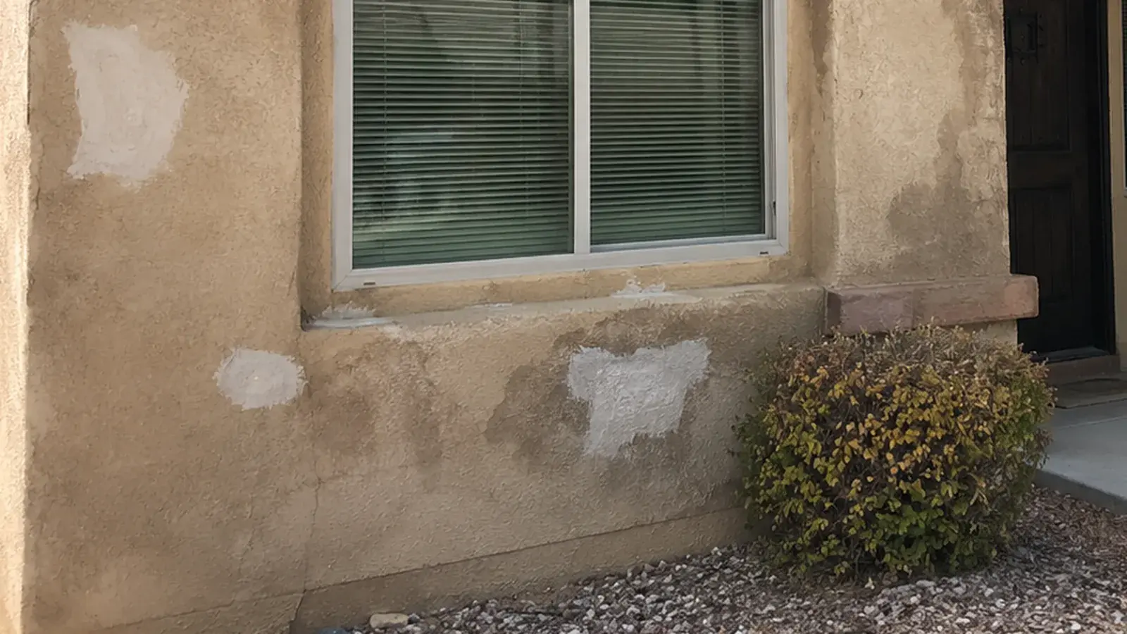 Stucco wall below a window showing pale patch repairs and discolouration, typical signs of moisture behind the finish