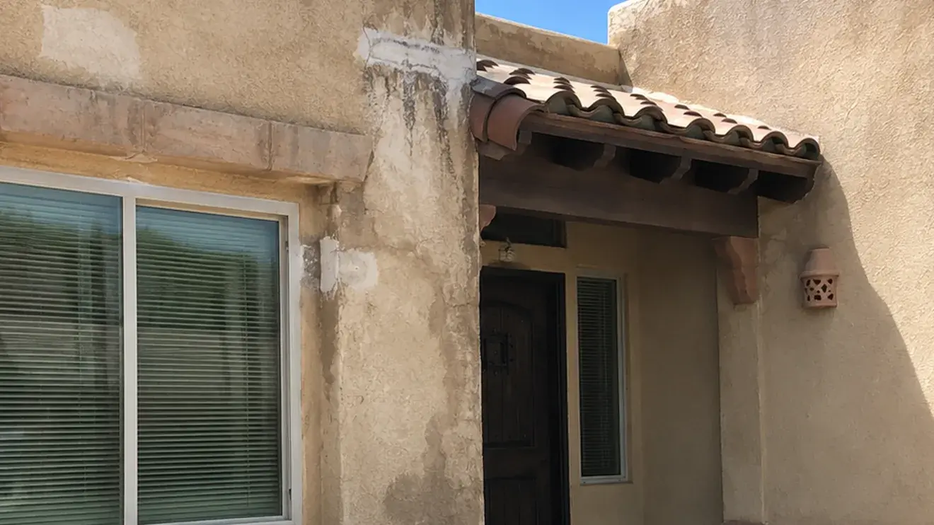 Dark water staining running down a stucco wall below the roofline and around a canale on a Las Cruces home