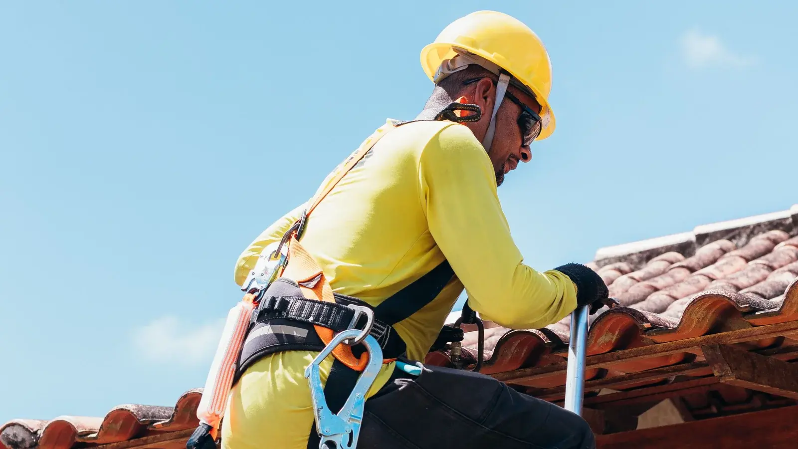 Roofer on a ladder inspecting the edge of a clay tile roof where it meets a stucco wall