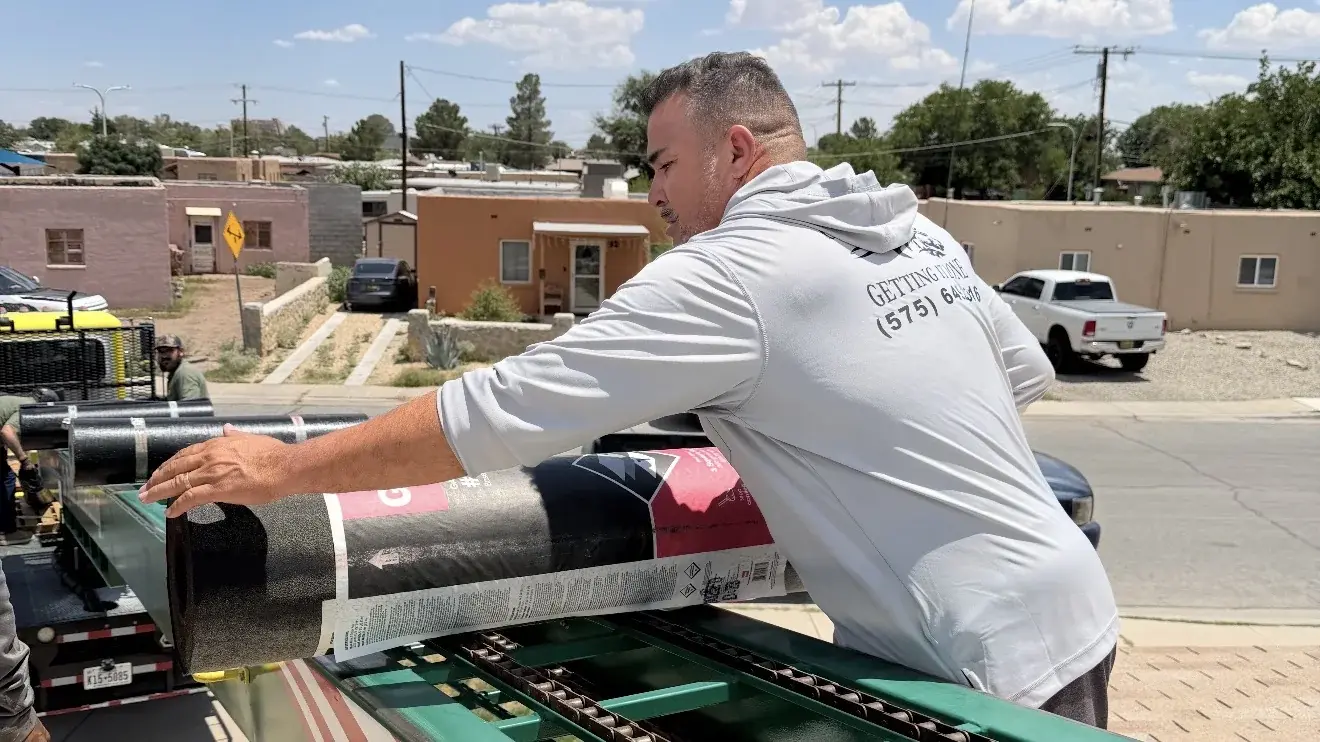 Roofing crew loading rolls of membrane onto a ladder hoist beside a white coated flat roof