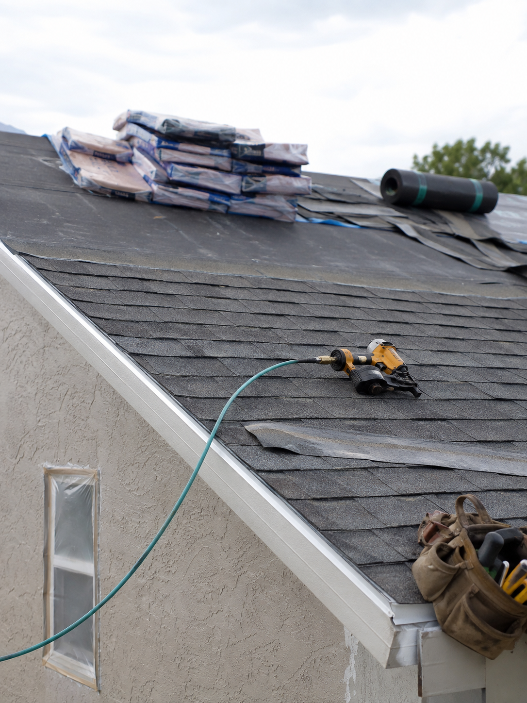 Roofing nail gun and materials staged on a shingle roof
