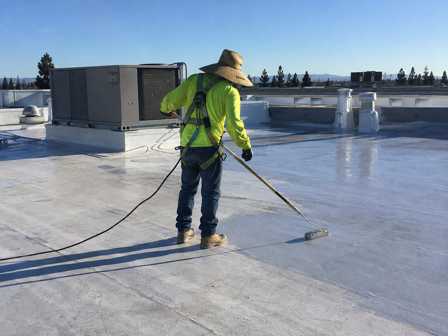 Worker applying reflective coating to a commercial flat roof