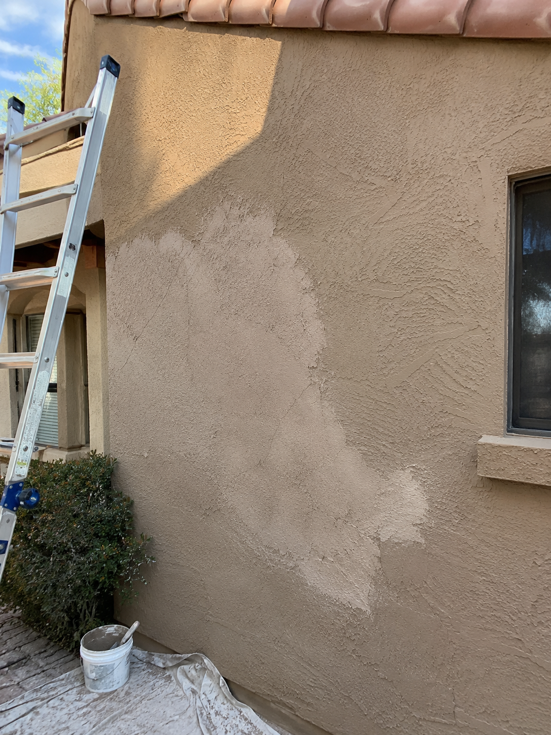 Stucco wall mid-repair with patched sections and a ladder