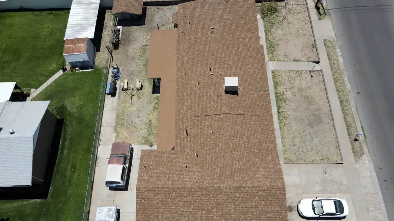 Overhead drone view of a completed brown shingle roof on a single-storey home with clean gutters and a clear driveway