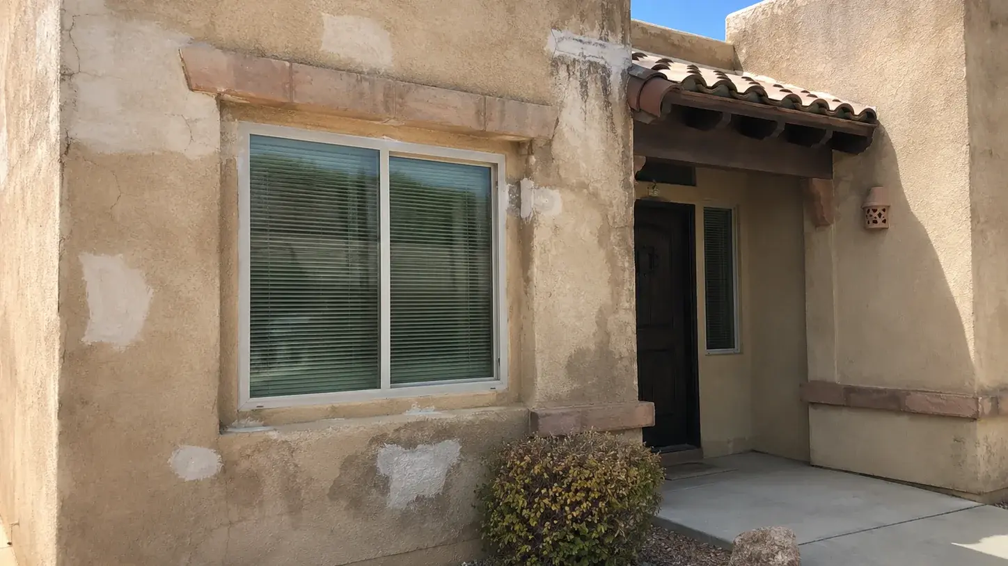 Weathered stucco wall on a Southwest home showing hairline cracks and pale patch repairs around a window