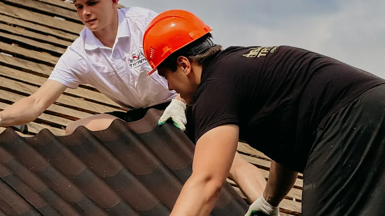 Two roofers in hard hats working along the ridge of a tile roof on a Las Cruces property