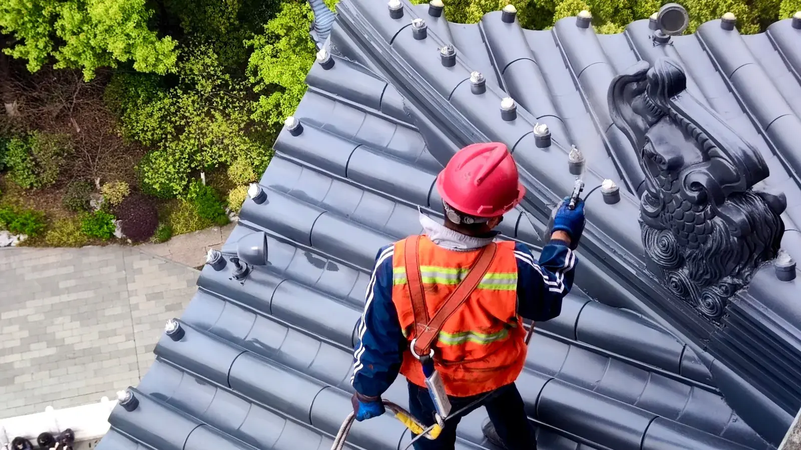 Roofer in a hard hat, safety vest and harness walking a tile roof during an inspection
