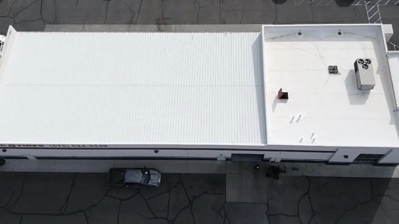 Overhead drone view of a commercial building with a white flat membrane roof, rooftop HVAC units, roof drains and a parapet edge