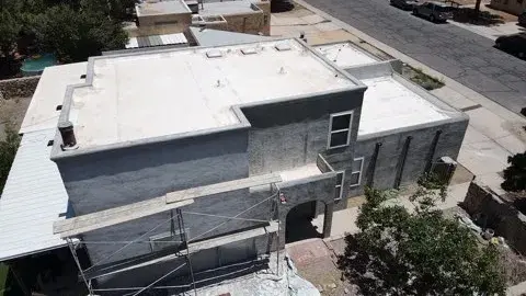 Aerial view of a two-story flat-roofed stucco building with parapet walls around the roof and scaffolding along one side