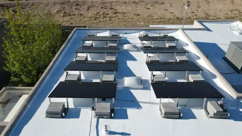 Drone view of a bright white coated flat roof with parapet walls and rows of rooftop solar panels