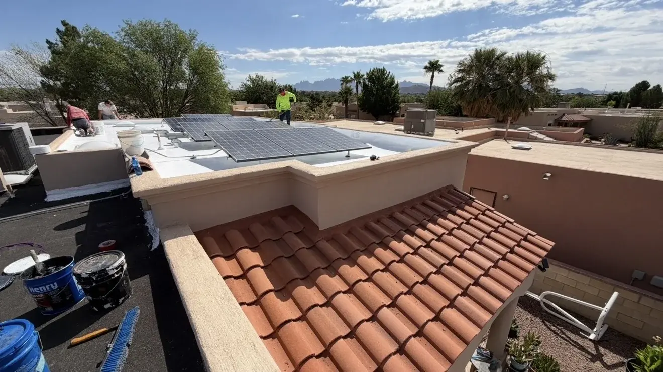 Stucco parapet walls surrounding a flat roof under coating work, with a tile roof below and the Organ Mountains behind