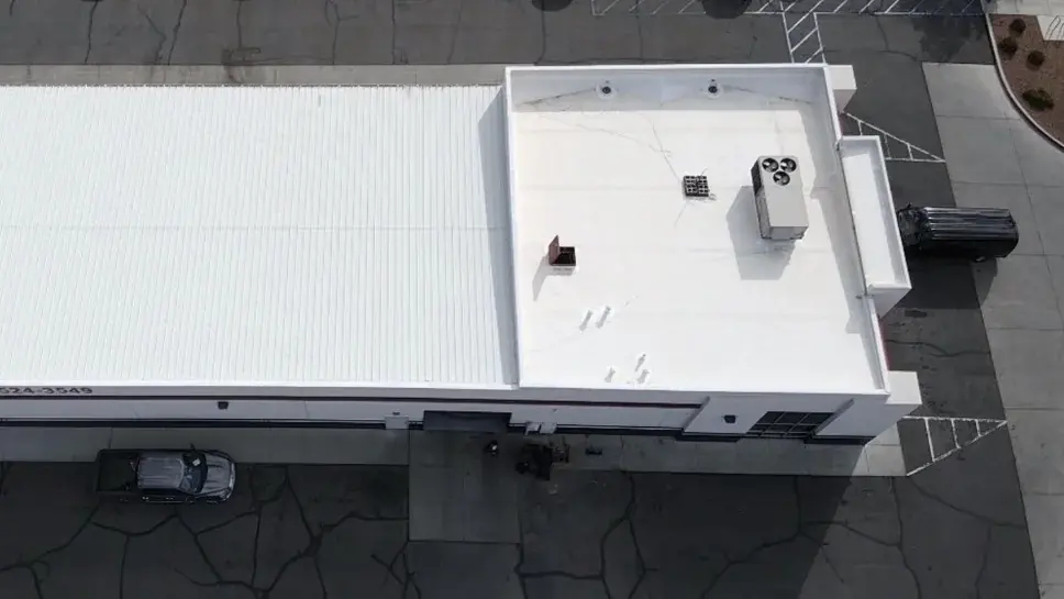 Aerial view of a commercial building with a white single-ply membrane flat roof, parapet edge and rooftop HVAC units